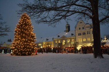 Das Bild zeigt einen vergangenen Rehauer Lebkuchenmarkt auf dem Maxplatz. Es ist der eingeschneite Maxplatz mit dem großen Weihnachtsbaum zu sehen, im Hintergrund ist das Alte Rathaus zu erkennen.