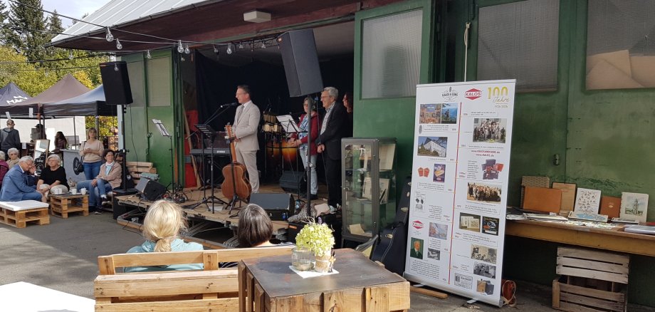 Auf dem Bild ist Bürgermeister Abraham neben Familie Hoffmann auf der Bühne zu sehen, davor befinden sich Sitzgelegenheiten und zahlreiche Besucher.