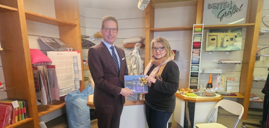 50 Jahre Betten Gräßel Der 1. Bürgermeister Michael Abraham beglückwünscht die Geschäftsinhaberin von Betten Gräßel, Marlene Kohrhammer, zum 50-jährigen Jubiläum und überreicht ein Geschenk.