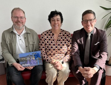 Auf dem Bild sind von links auf einem Sofa sitzend zu sehen: Zahnarzt Fabian Döhler, Zahnärztin Dr. Heike Ronneburg und Bürgermeister Michael Abraham