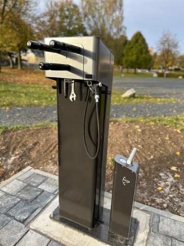 Auf dem Bild ist die neue Fahrrad-Service-Station zu sehen. Links ist ein größerer Aufbau mit Zubehörteilen sowie einer Halterung für Fahrräder, links befindet sich die Pumpe für die Luftpumpe.