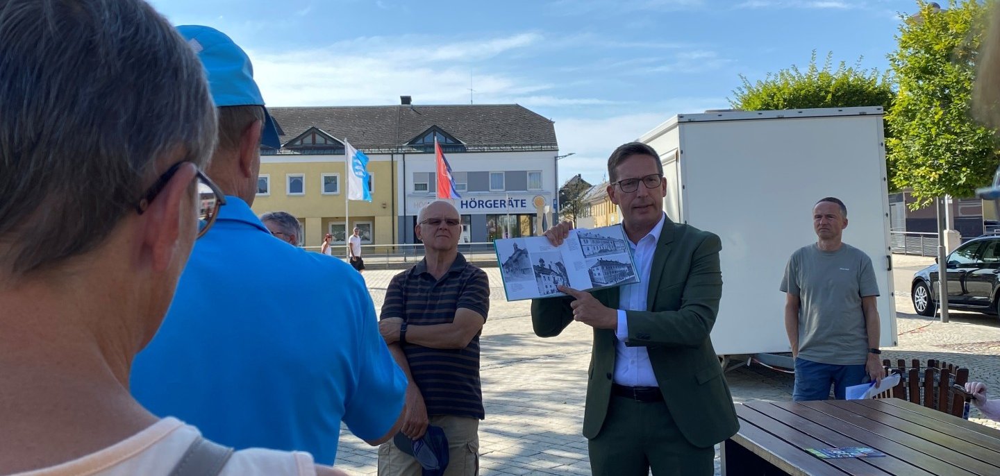 Auf dem Bild ist Bürgermeister Michael Abraham zu sehen, wie er den Besuchern eines Stadtspaziergangs interessante Informationen mit Bildmaterial näher bringt.
