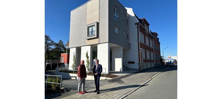 Auf dem Bild stehen Matthias Stingl (links) mit Bürgermeister Michael Abraham vor dem sanierten Gebäude Geothestraße 25. Dahinter ist das neu gebaute Einfamilienhaus zu erkennen.