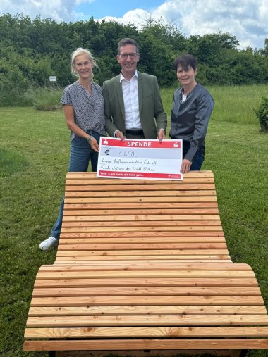 Das Bild zeigt Bürgermeister Abraham zwischen der Vorsitzenden Iris Hauenstein-Busch (links) und 2. Vorsitzenden Melanie Müller-Winterling (rechts) mit dem symbolischen Scheck vor einem der beiden neuen Waldsofas.