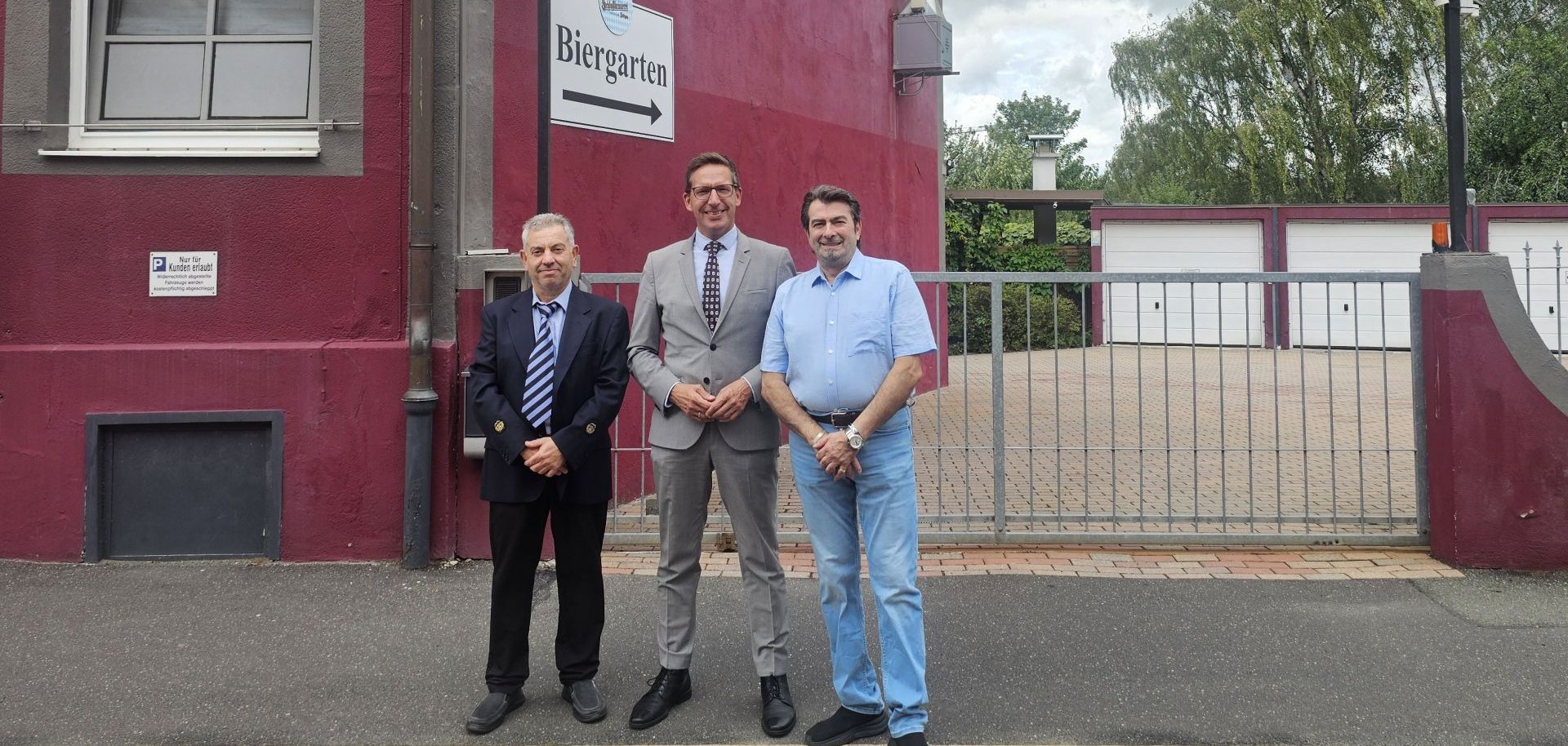Auf dem Bild sind die neuen Pächter des italienischen Restaurants in der Unlitzstraße (ehemals Da Pippo) mit Bürgermeister Michael Abraham vor dem dunkelroten Gebäude und dem Eingang zum Biergarten des "Ristorante Pizzeria Da Mario e Nicola" zu sehen.