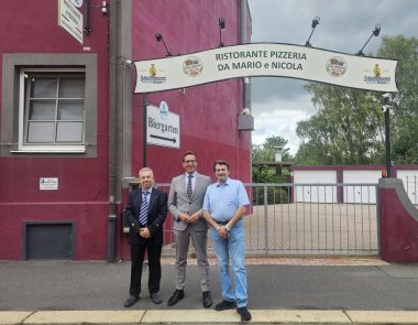 Auf dem Bild sind die neuen Pächter des italienischen Restaurants in der Unlitzstraße (ehemals Da Pippo) mit Bürgermeister Michael Abraham vor dem dunkelroten Gebäude und dem Eingang zum Biergarten des "Ristorante Pizzeria Da Mario e Nicola" zu sehen.