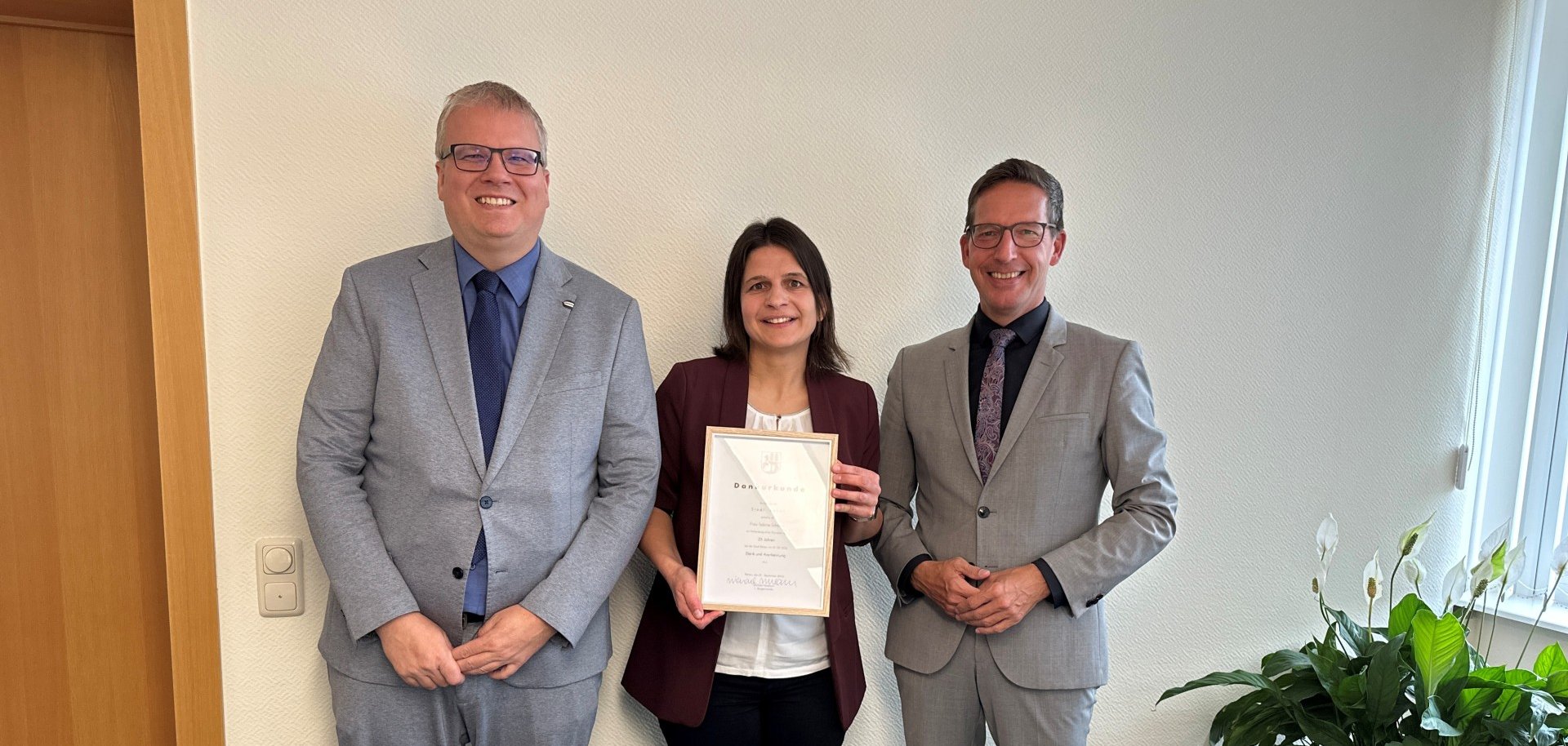 Das Bild zeigt Jubilarin Sabine Schödel mit ihrer Urkunde in der Hand zwischen Ordnungsamtsleiter und Personalratsvorsitzendem Frank Rameckers (links) und Erstem Bürgermeister Michael Abraham (rechts).