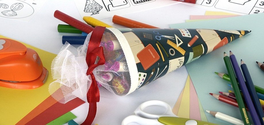 Das Bild zeigt eine kleine Zuckertüte auf einem Tisch liegen, auf welchem noch Stifte und weitere Schreibmaterialien für die Schule verteilt sind.