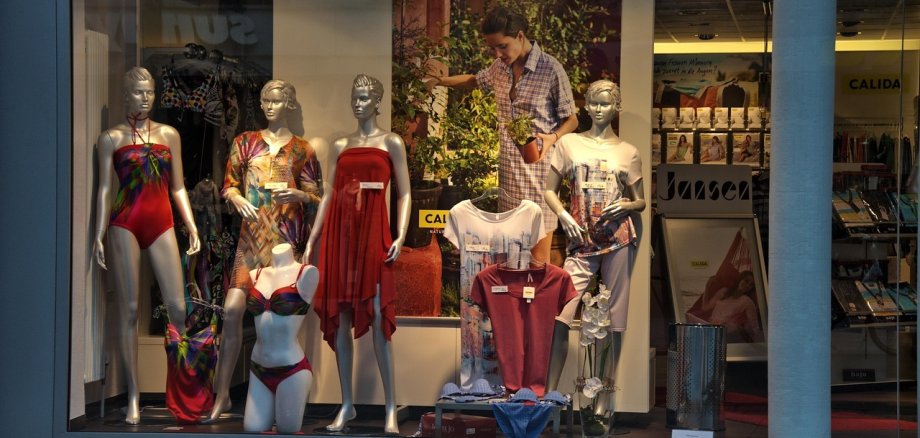 Das Bild zeigt ein Schaufenster mit Puppen und unterschiedlichen Artikeln wie Pullover, Mützen, Hosen usw.