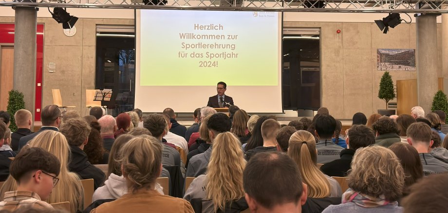 Das Bild zeigt Bürgermeister Abraham am Rednerpult vor den Sportlern.