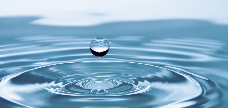 Das Bild zeigt einen Wassertropfen, der sich gerade aus dem Wasser unten erhoben hat.