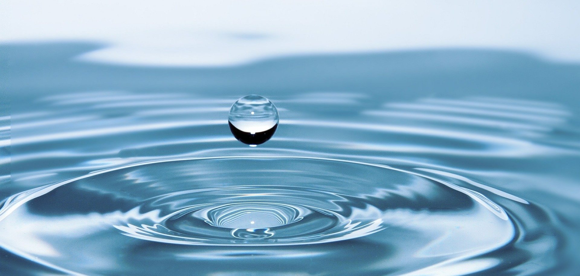 Das Bild zeigt einen Wassertropfen, der sich gerade aus dem Wasser unten erhoben hat.