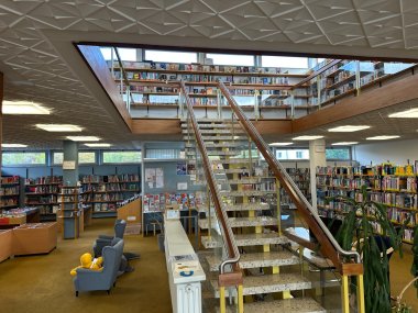 Das Bild zeigt die Räumlichkeiten der Bücherei. Mittig ist die Treppe nach oben, links der Kinderbereich und rechts Bücher für Erwachsene.