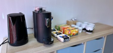 Auf dem Bild sind ein Wasserkocher, eine Kaffeemaschine sowie Tassen, Kapseln und Tees zu sehen.
