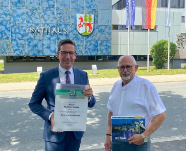 Das Bild zeigt Bürgermeister Michael Abraham neben Matthias Lottes, der den Rehauer Stadtrat zum 30.04.2026 verlassen hat, während er ihm eine Dankurkunde sowie ein kleines Präsent übergeben hat.