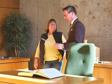 Auf dem Bild sind Christa Eckardt und Bürgermeister Michael Abraham zu sehen. Frau Eckardt bekommt eine Urkunde von Bürgermeister Abraham überreicht. Im Vordergrund ist zudem das Goldene Buch der Stadt Rehau zu sehen, in welches sich Frau Eckardt im Anschluss eingetragen hat.
