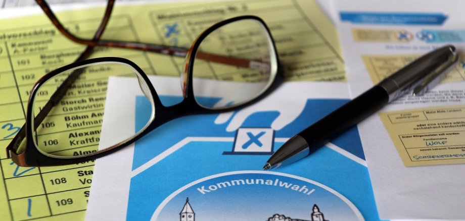 Auf dem Bild sind Wahlunterlagen zur Kommunalwahl, eine Lesebrille und ein Kugelschreiber zu sehen