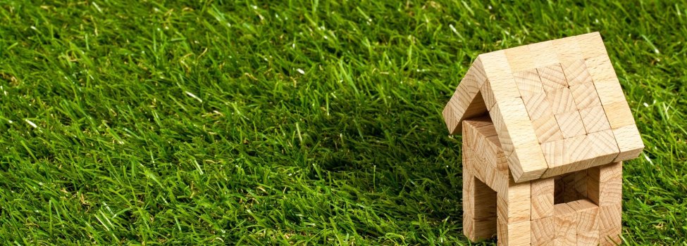 Das Bild zeigt ein Holz-Haus, welches aus vielen kleinen Holz-Würfeln besteht. Es befindet sich auf einer grünen Wiese.
