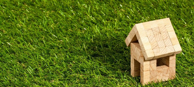 Das Bild zeigt ein Holz-Haus, welches aus vielen kleinen Holz-Würfeln besteht. Es befindet sich auf einer grünen Wiese.