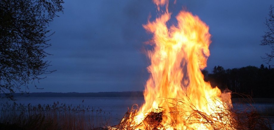 Das Bild zeigt ein Feuer, welches vor einem See aufgebaut wurde.