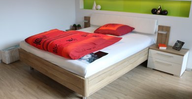 Auf dem Bild ist ein Bett und zwei Nachttische zu erkennen. Auf dem Bett ist eine rote Bettwäsche frisch zusammengelegt.