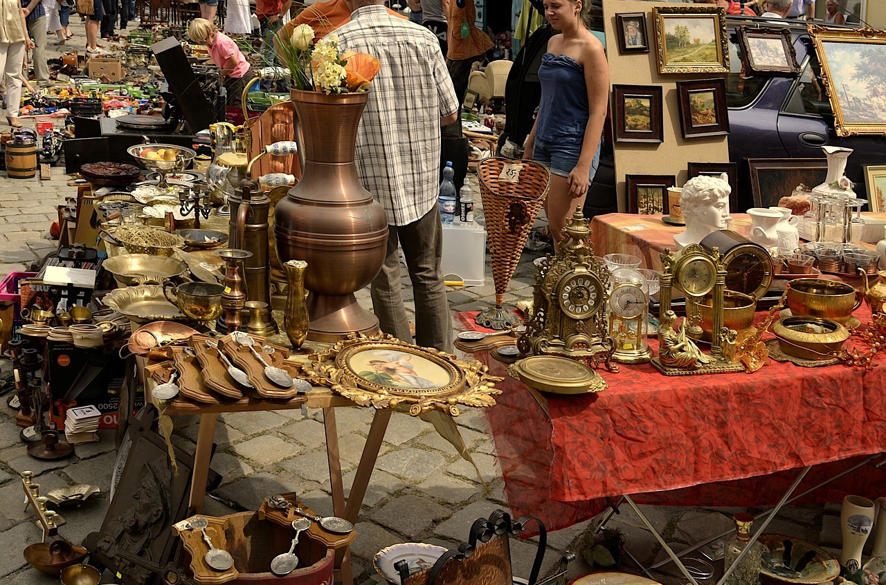 Das Bild zeigt mehrere Flohmarkt-Stände mit Trödel-Artikeln wie alte Standuhren, Silberlöffel oder Bilder mit hochwertigen Rahmen.