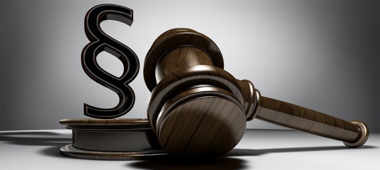 Das Bild zeigt einen Hammer, welchen Richter für gewöhnlich verwenden, der auf dem Tisch liegt. Auf dem dazugehörigen Sockel steht ein Paragrafen-Zeichen.