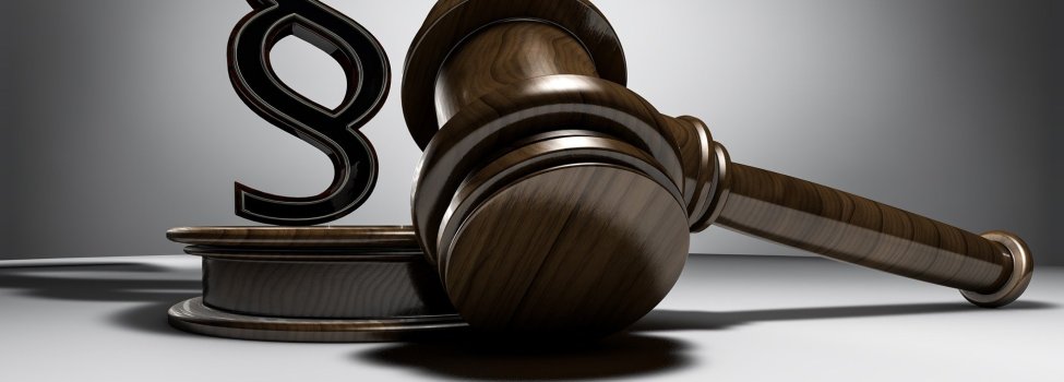 Das Bild zeigt einen Hammer, welchen Richter für gewöhnlich verwenden, der auf dem Tisch liegt. Auf dem dazugehörigen Sockel steht ein Paragrafen-Zeichen.