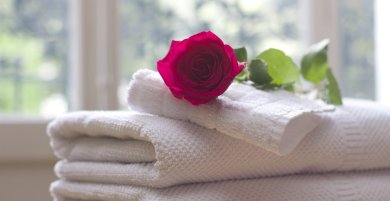 Das Bild zeigt eine rote Rose auf weißen, ordentlich zusammengelegten Handtüchern.