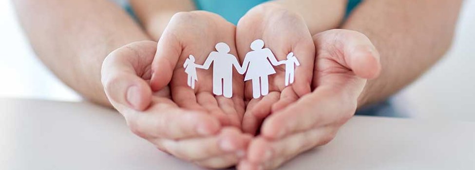 Das Bild zeigt vier Hände: Unten liegen die größeren Hände, vermutlich eines Mannes, nebeneinander mit den Handinnenflächen nach oben. Darüber sind ebenso zwei Hände nebeneinander gelegt. In den oberen Handinnenflächen befindet sich ein Papierzuschnitt, der eine Familie darstellen soll.