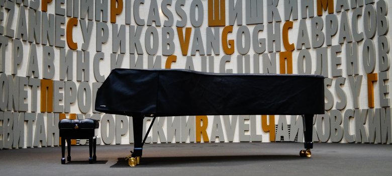 Das Bild zeigt einen abgedeckten Flügel in der Mitte eines Raumes. Davor befindet sich der entsprechende Hocker für den Pianisten.