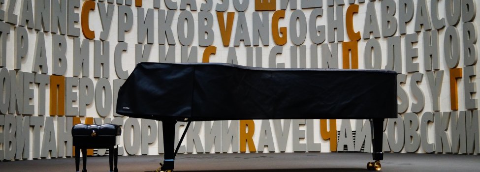 Das Bild zeigt einen abgedeckten Flügel in der Mitte eines Raumes. Davor befindet sich der entsprechende Hocker für den Pianisten.