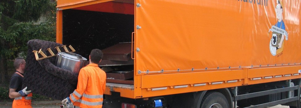 Auf dem Bild ist eine Müllabfuhr zu sehen. Dahinter stehen zwei Männer und legen alte Möbel hinein.