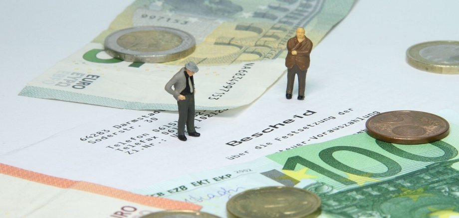 Auf dem Bild sind zwei Spielfiguren zu sehen. Unter den zwei Spielfiguren ist Geld.