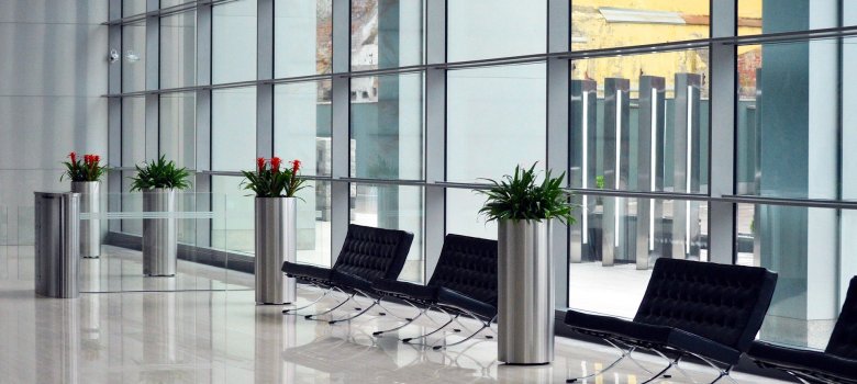 Auf dem Bild ist ein Raum zu sehen. In dem Raum sind Stühle und Pflanzen, außerdem eine Glasfront.