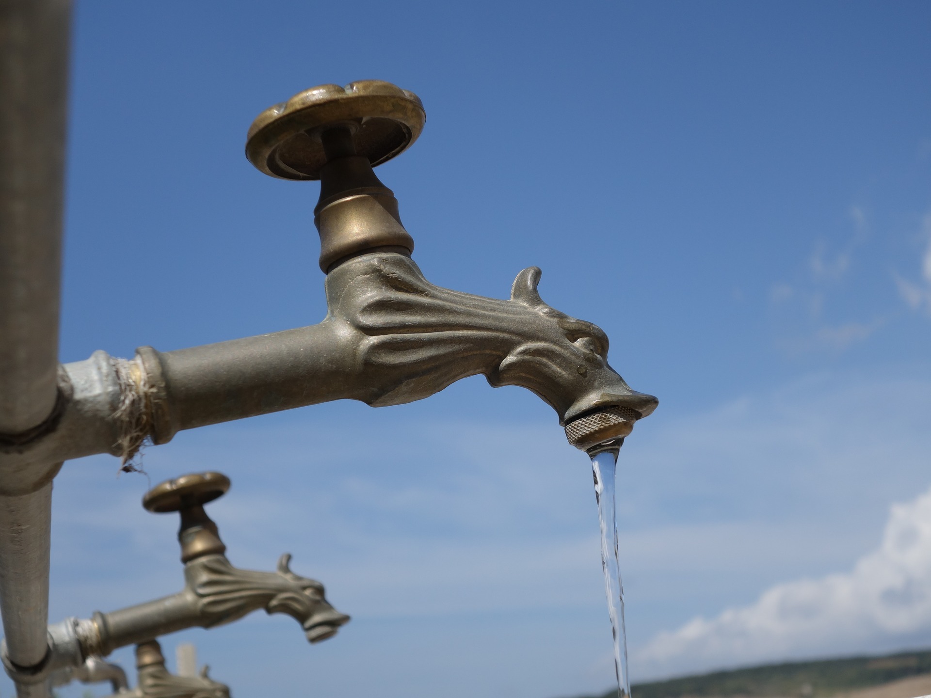 Auf dem Bild ist ein Wasserhahn im Außenbereich zu sehen, der gerade aufgedreht ist.