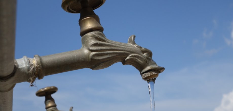 Auf dem Bild ist ein Wasserhahn im Außenbereich zu sehen, der gerade aufgedreht ist.
