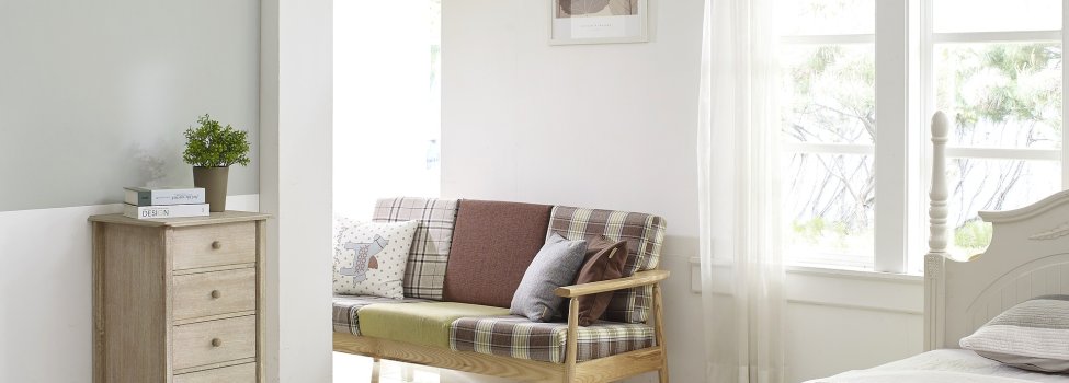 Auf dem Bild ist ein heller Wohnraum mit Bett und Sitzbank zu sehen.