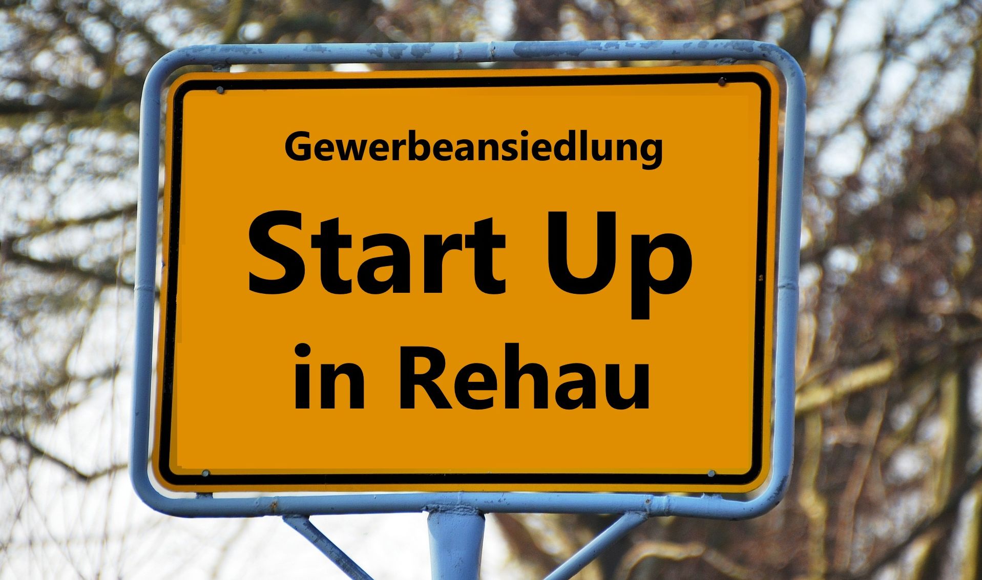 Das Bild zeigt ein Ortsschild, auf welchem der folgende Text steht: "Gewerbeansiedlung Start Up in Rehau".