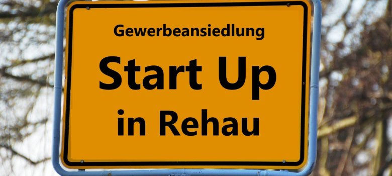 Das Bild zeigt ein Ortsschild, auf welchem der folgende Text steht: "Gewerbeansiedlung Start Up in Rehau".