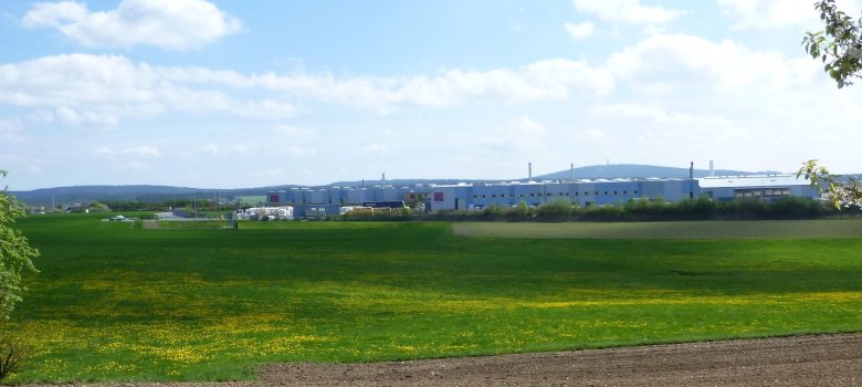 Das Bild zeigt vordergründig eine große Wiese. Im Hintergrund ist eine Halle der Firma LAMILUX zu erkennen.