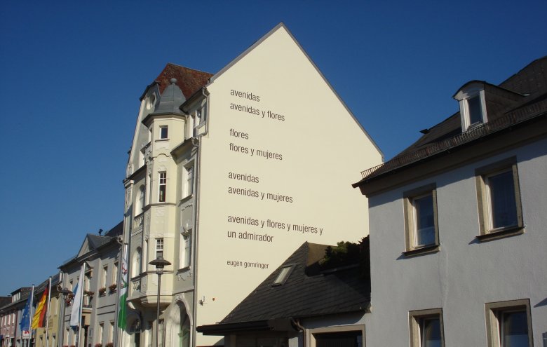 Das Bild zeigt das Anwesen Maxplatz 5 von außen. Darauf ist seitlich das Gedicht "avenidas" von Eugen Gomringer zu erkennen.