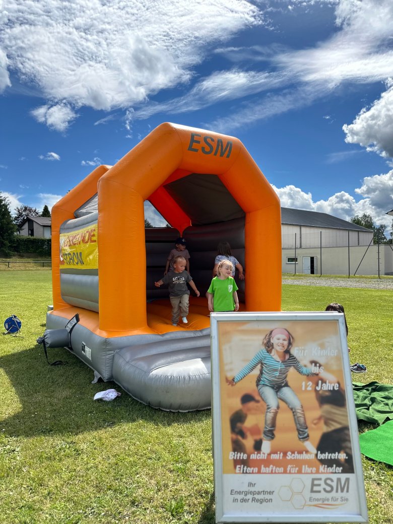 Das Bild zeigt eine orangene Hüpfburg der ESM, welche an einem Familien- und Vereinsfest im Rehauer Jahnstadion aufgebaut war.