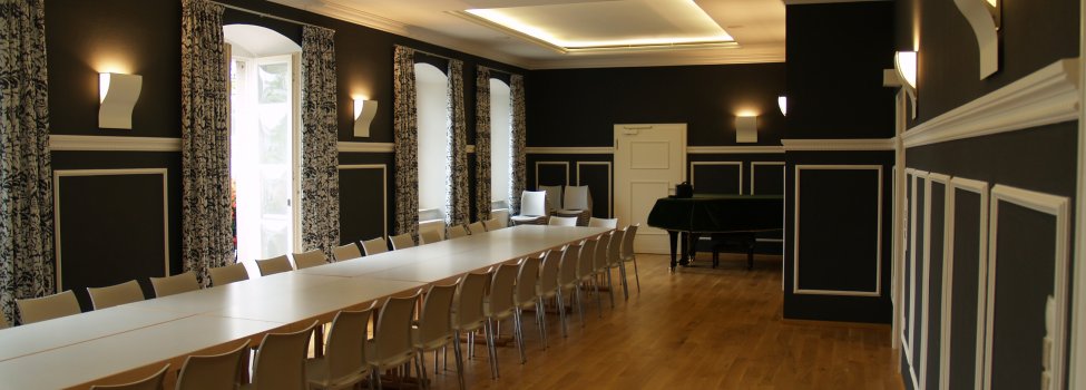 Das Bild zeigt den Festsaal im Alten Rathaus Rehau. Darin befinden sich einige Tische, welche eine lange Tafel ergeben, sowie Stühle außen herum. Dahinter befindet sich ein Flügel.