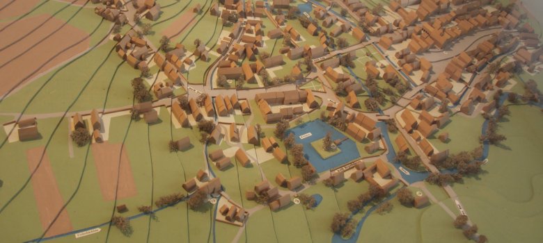 Das Bild zeigt ein Stadtmodell von Rehau, welches Rehau vor vielen Jahren abbildet. Zu erkennen sind Gewässer, Häuser, Bäume und damalige Wege.