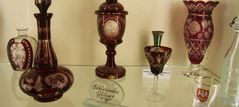 Auf dem Bild sind verschiedene Glas-Artikel in einer Vitrine zu sehen. Die meisten Gegenstände sind mir roter Farbe verarbeitet. Es handelt sich um Gegenstände der Schlesischen Sammlung.