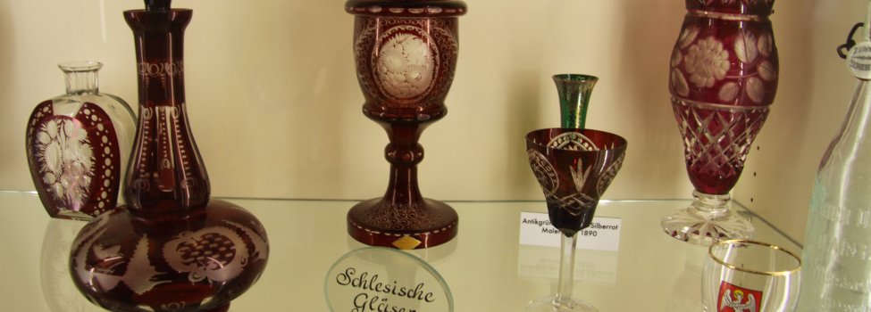 Auf dem Bild sind verschiedene Glas-Artikel in einer Vitrine zu sehen. Die meisten Gegenstände sind mir roter Farbe verarbeitet. Es handelt sich um Gegenstände der Schlesischen Sammlung.