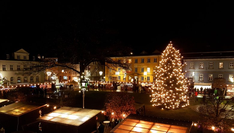 Das Bild zeigt den Rehauer Lebkuchenmarkt vom Balkon des Festsaals im Alten Rathaus aus. Zu sehen ist der große Weihnachtsbaum mit seinen Lichtern und viele Holzbuden der Anbieter des Marktes. Auch einige Besucher sind zu erkennen.