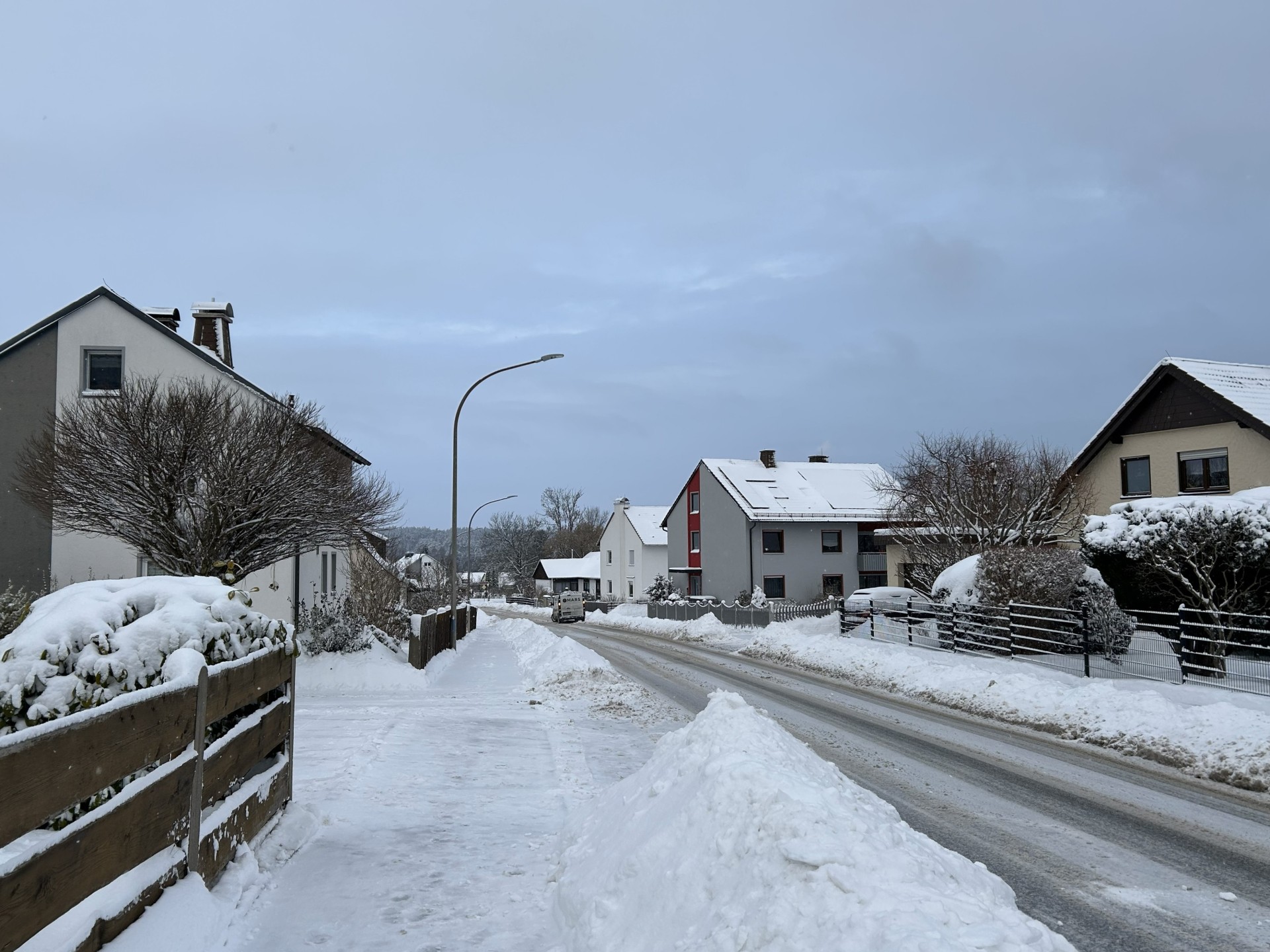 Das Bild zeigt eine Straße in Rehau mit Schneehäufen. Mittig ist ein gut geschorter Gehsteig zu sehen.