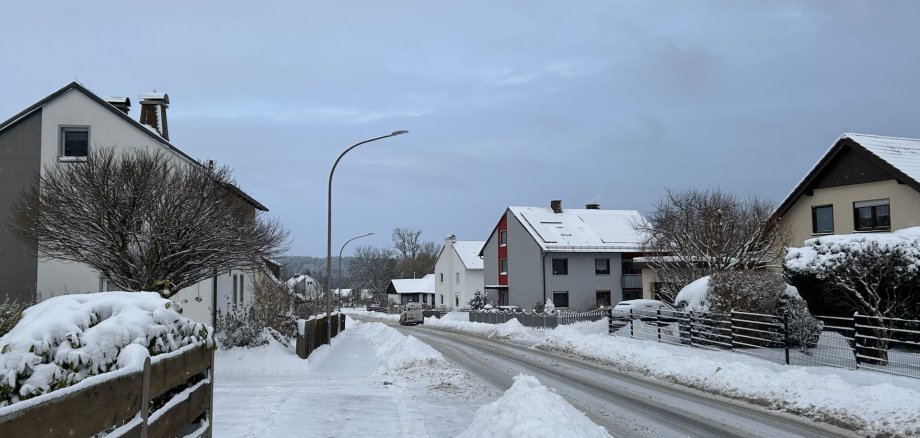 Das Bild zeigt eine Straße in Rehau mit Schneehäufen. Mittig ist ein gut geschorter Gehsteig zu sehen.